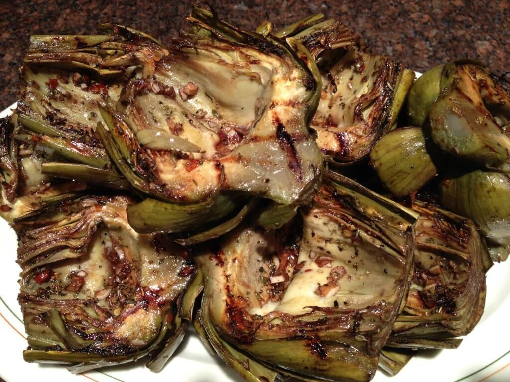 Grilled artichoke halves with herbs and spices on a white plate.
