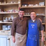 Two smiling men in aprons standing in front of shelves in La Baldigara.
