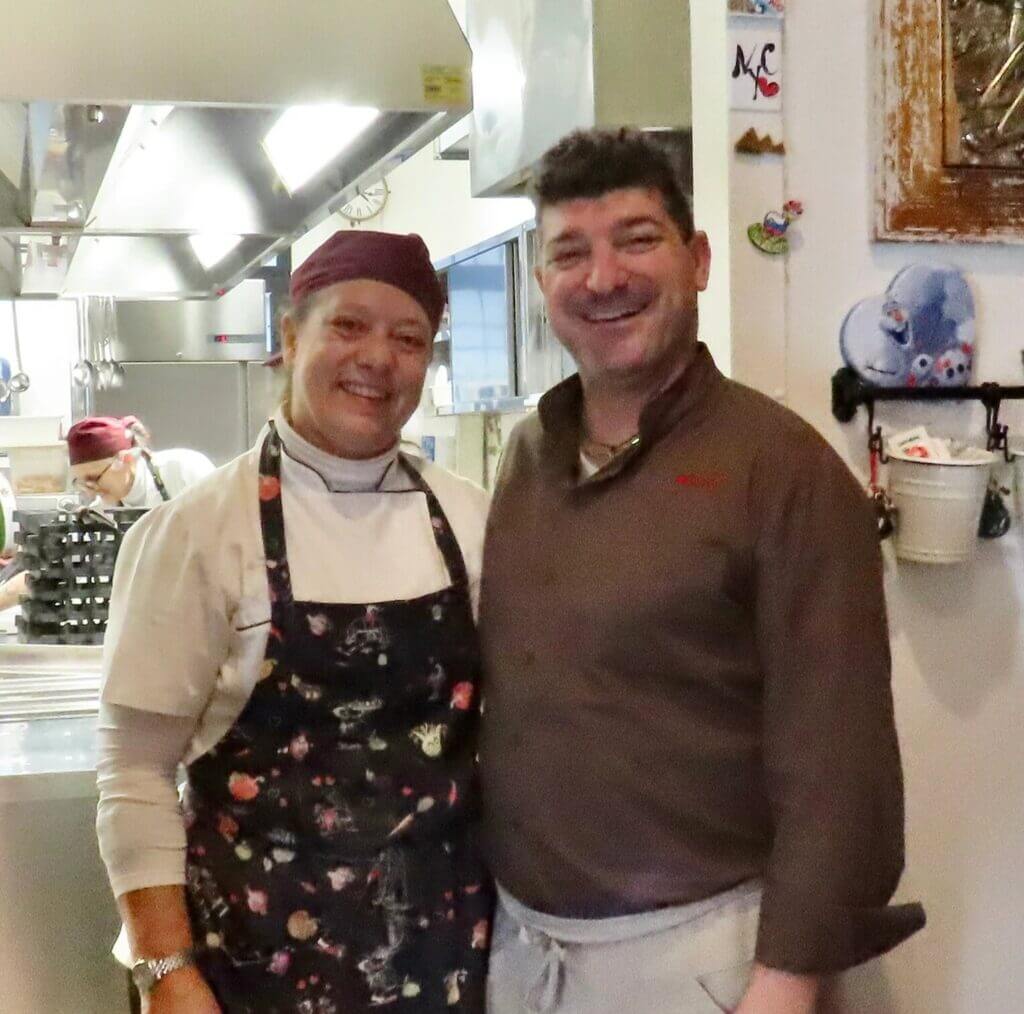 Two chefs smiling in a kitchen, one wearing a La Baldigara apron.