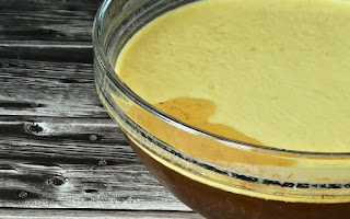 Close-up of a glass bowl showing a layer of fat floating on top of a rich, dark broth against a rustic wooden background.