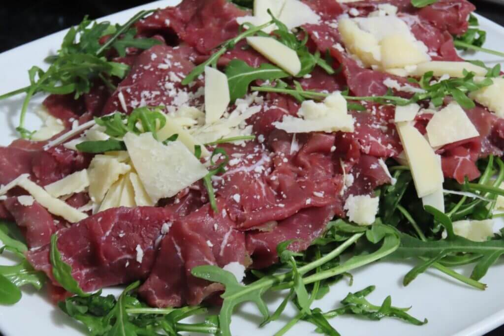 Carpaccio with arugula and parmesan cheese on a white plate. Italian appetizer.