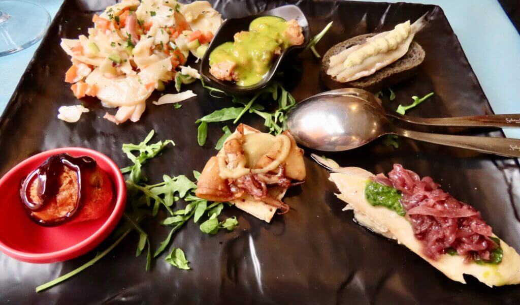 Assorted tapas on a black plate, including seafood salad and anchovies.